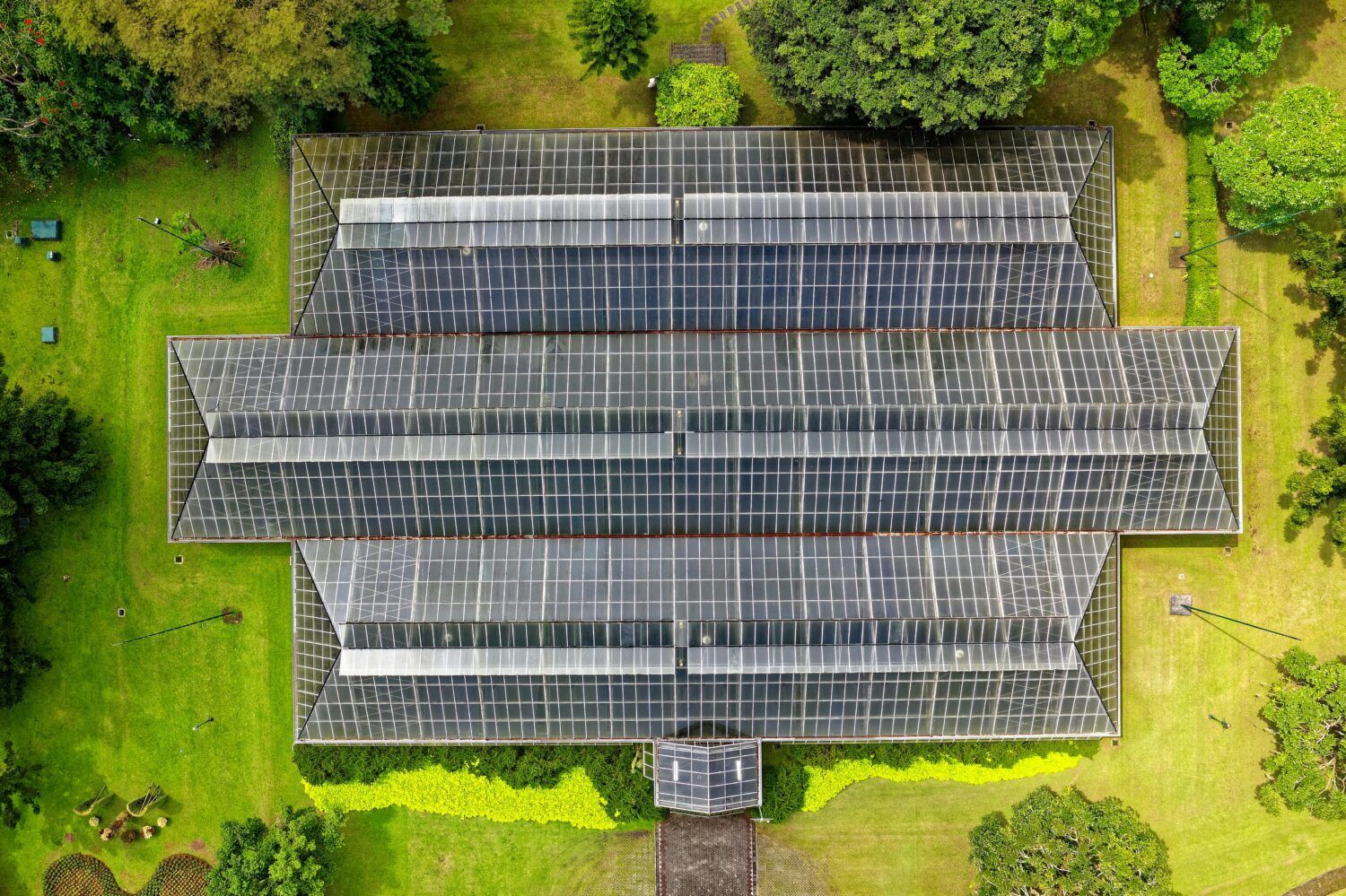 Aerial view of a large solar-paneled roof surrounded by green grass and trees.