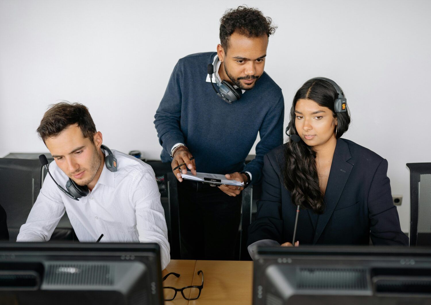 Three coworkers reviewing documents at desks with computer monitors in an office