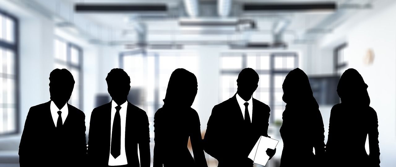 Silhouetted business people standing in a bright office hallway, one holding papers