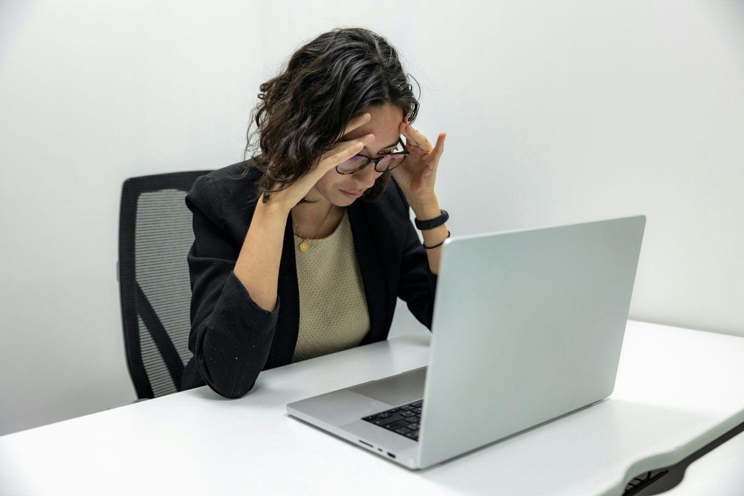Person at a desk with laptop, holding their head in frustration while working in an office