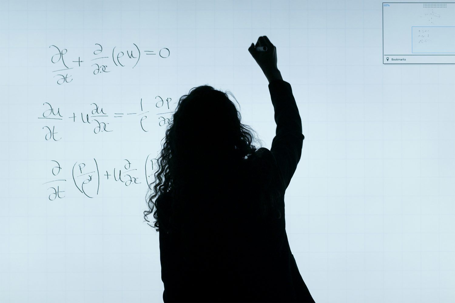 Silhouette of a person writing equations on a whiteboard in a classroom or lecture setting