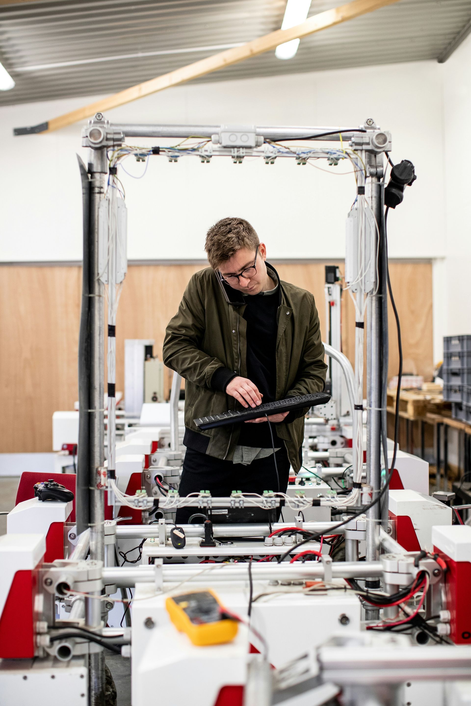 Technician adjusting a machine in a workshop, surrounded by metal frames and equipment.