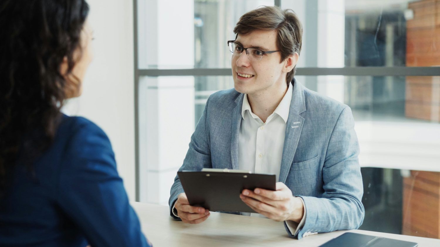 Two people in a bright office discuss a document on a tablet across a table