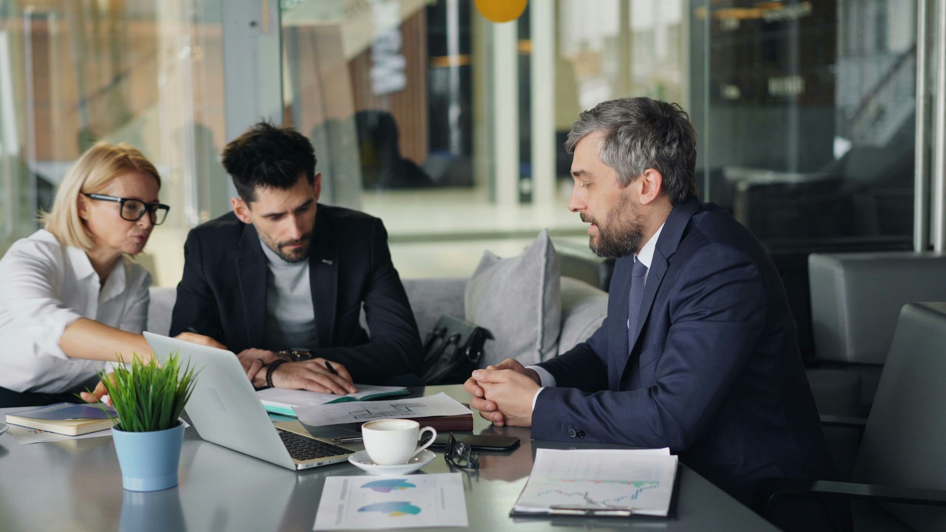 Three businesspeople in a meeting around a laptop in a bright office lounge