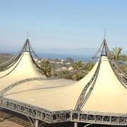 Due tende beige con struttura in metallo, con vista su una città costiera, sotto un cielo azzurro.