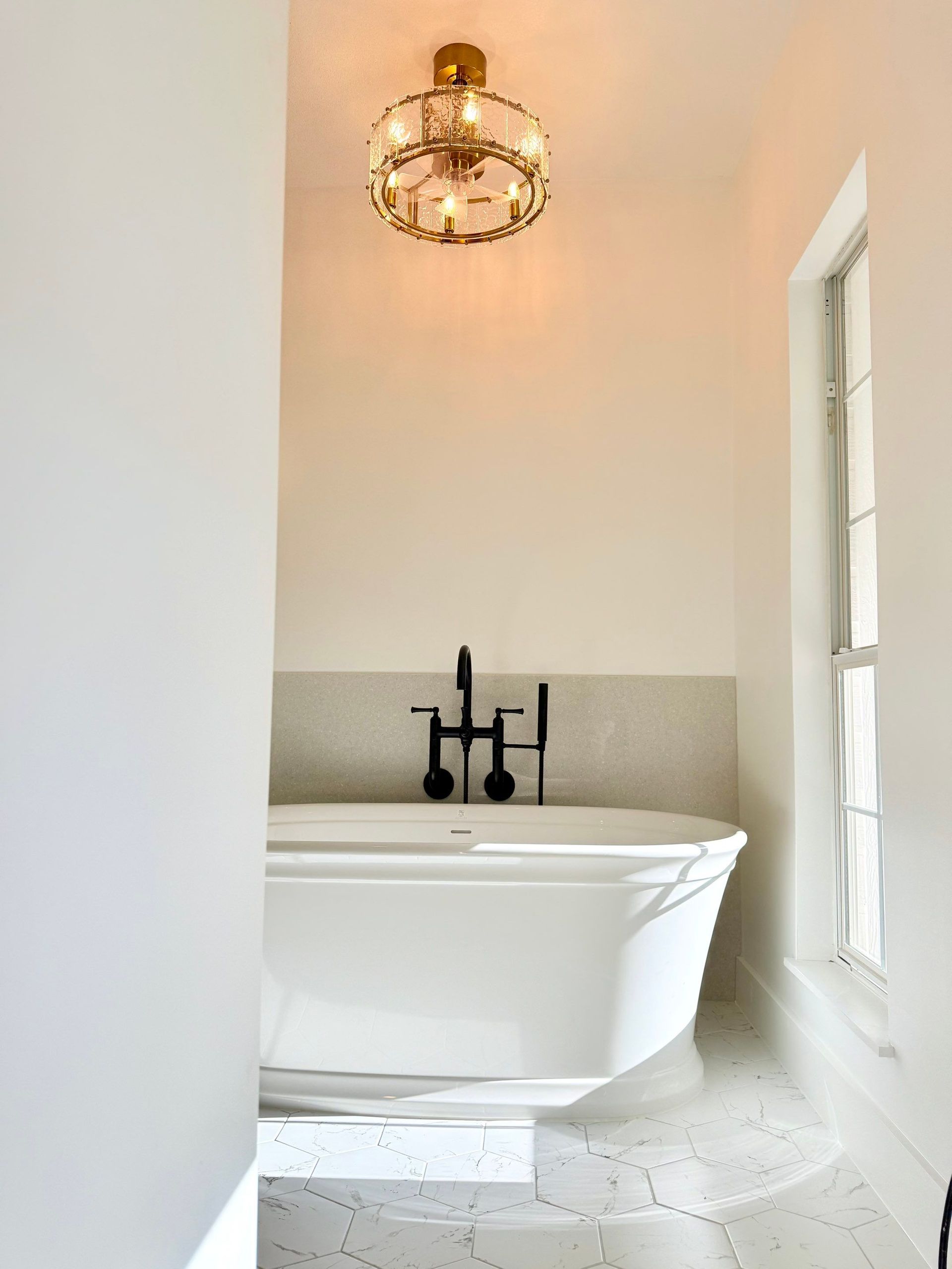 White bathroom with a freestanding tub, black faucet, and gold chandelier.