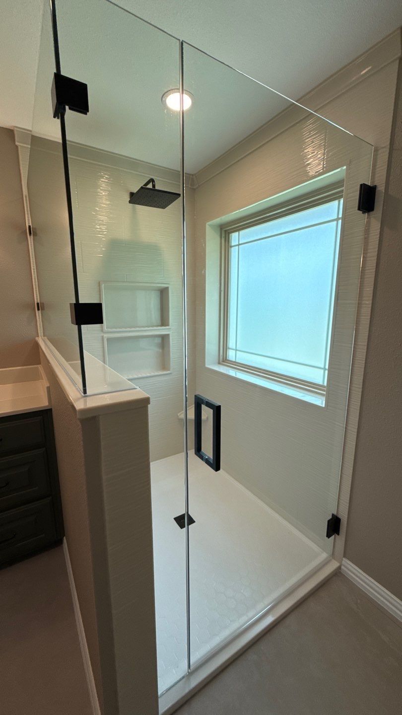 ADA Custom Walk In Shower w/ Glass shower enclosure with black hardware, white walls, and a window.