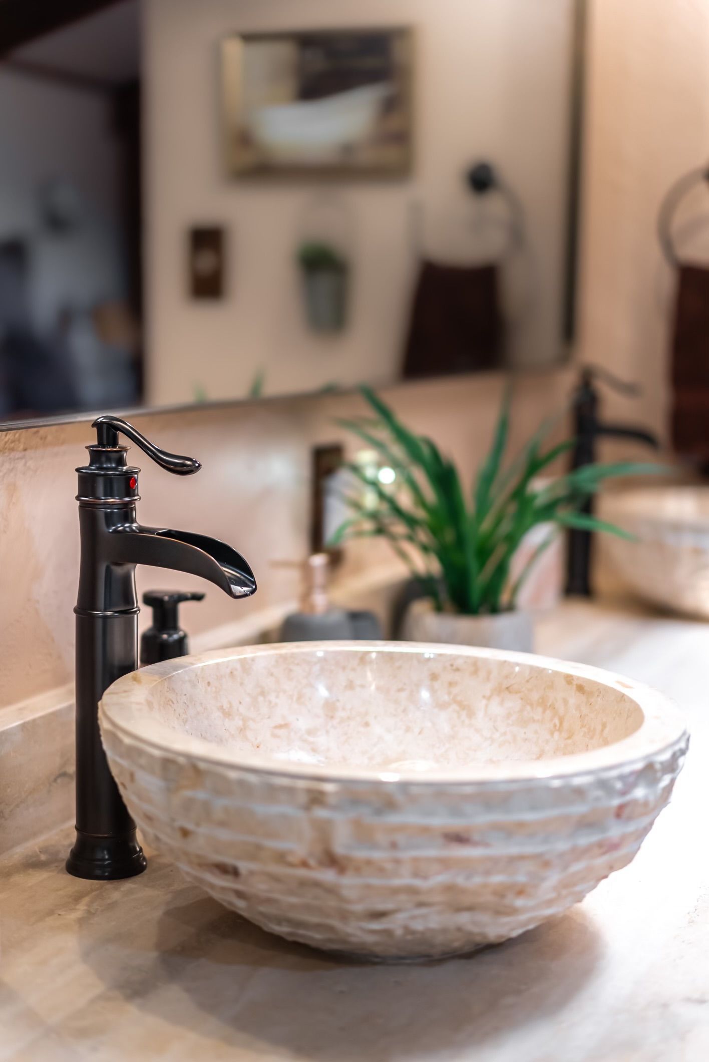 Bathroom sink with a stone bowl, black faucet, and greenery.