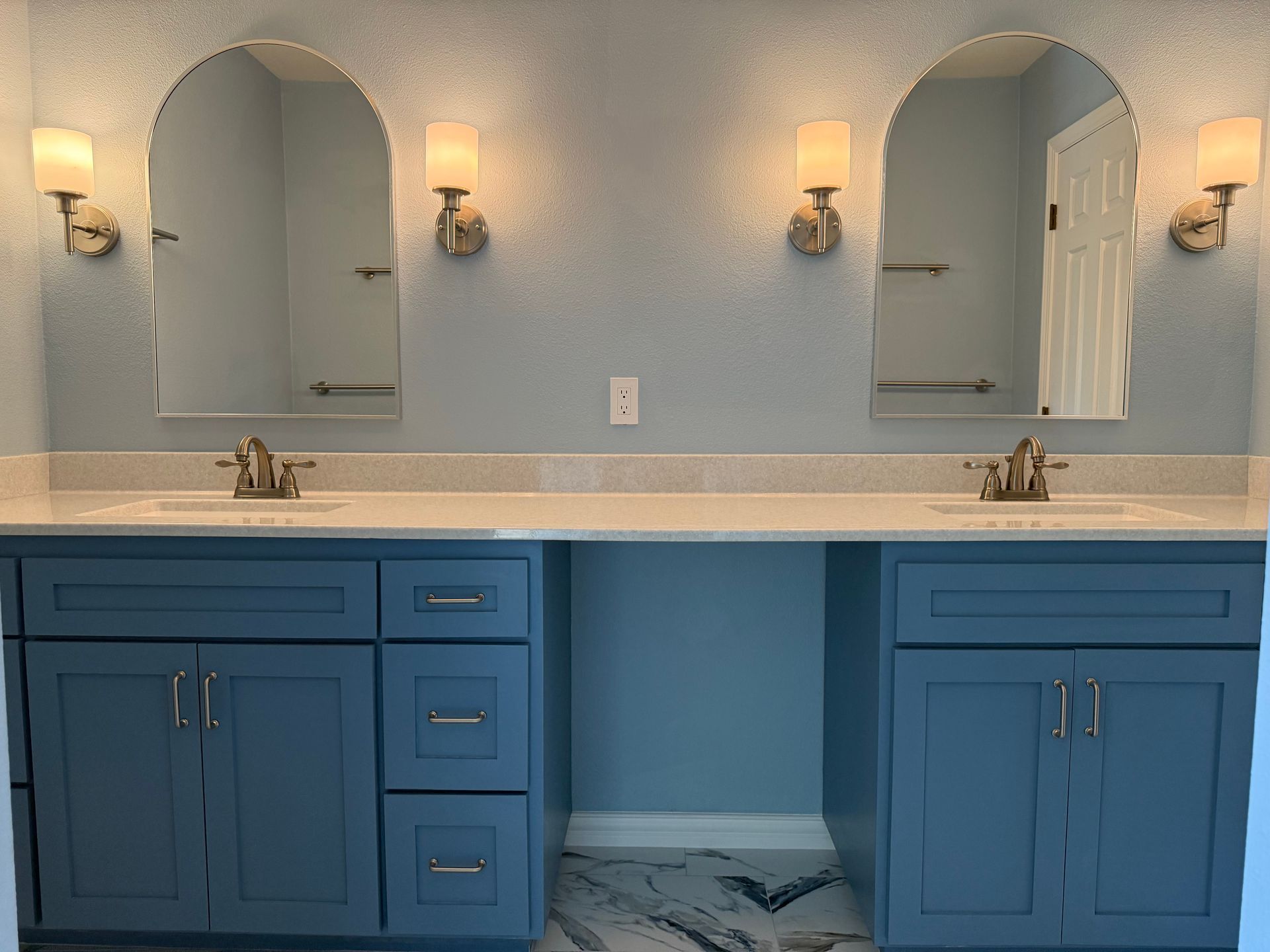 Two-sink bathroom with blue cabinets, arched mirrors, and sconce lighting.