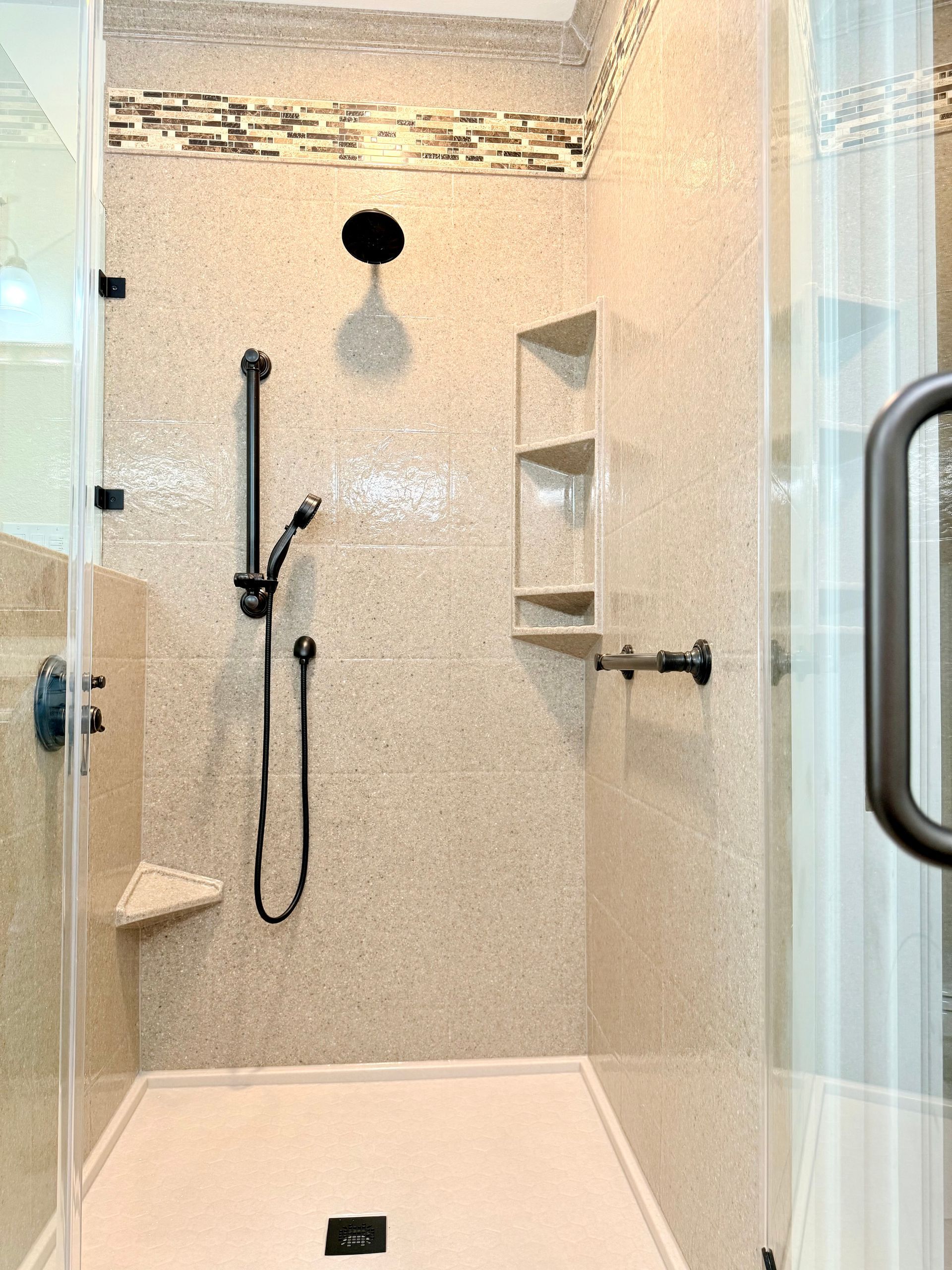 Shower with beige tile, black shower fixtures, glass door, and built-in shelves.