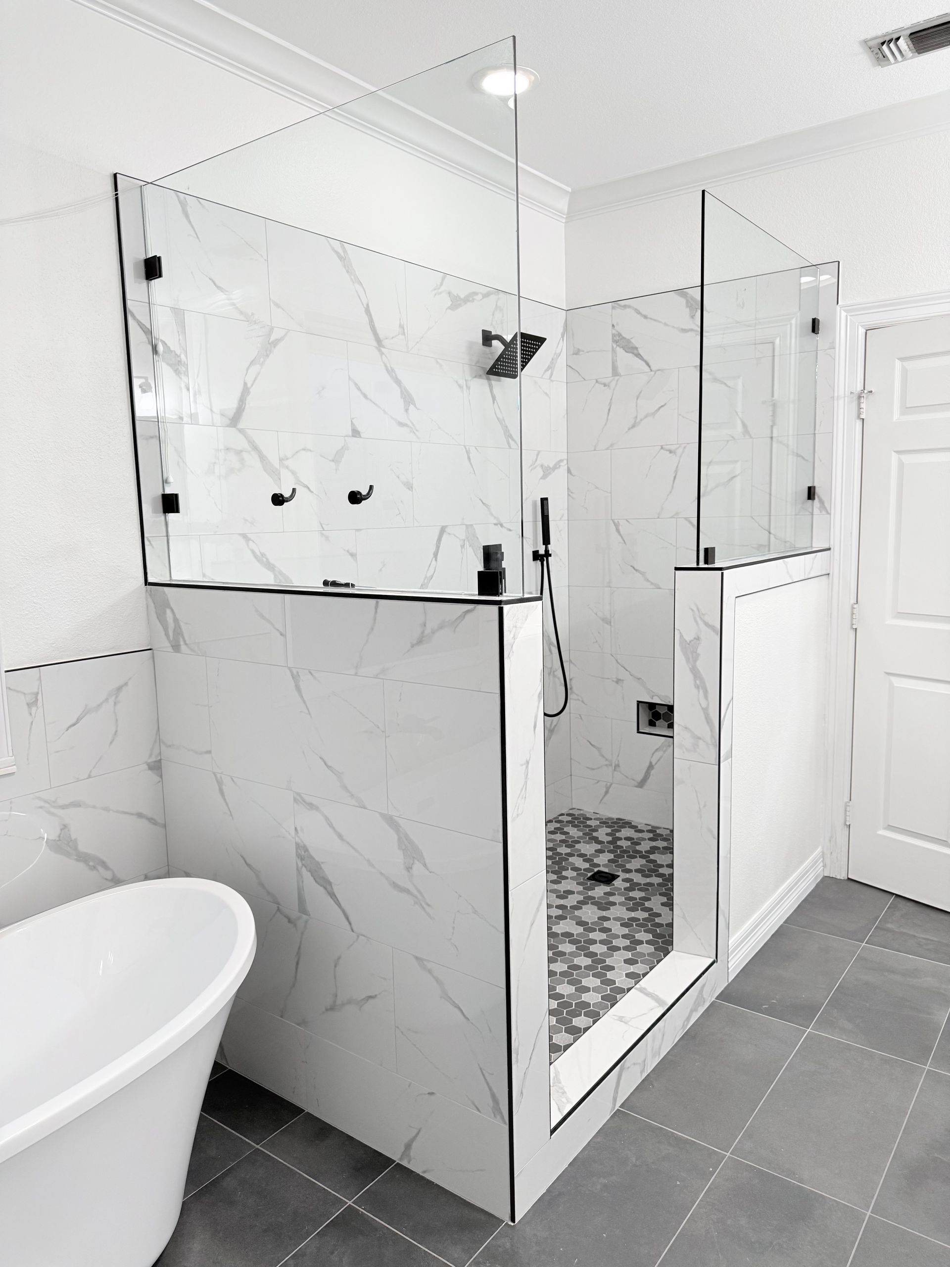 Modern bathroom with walk-in shower. Marble-like tile, glass panels, and a standalone tub.