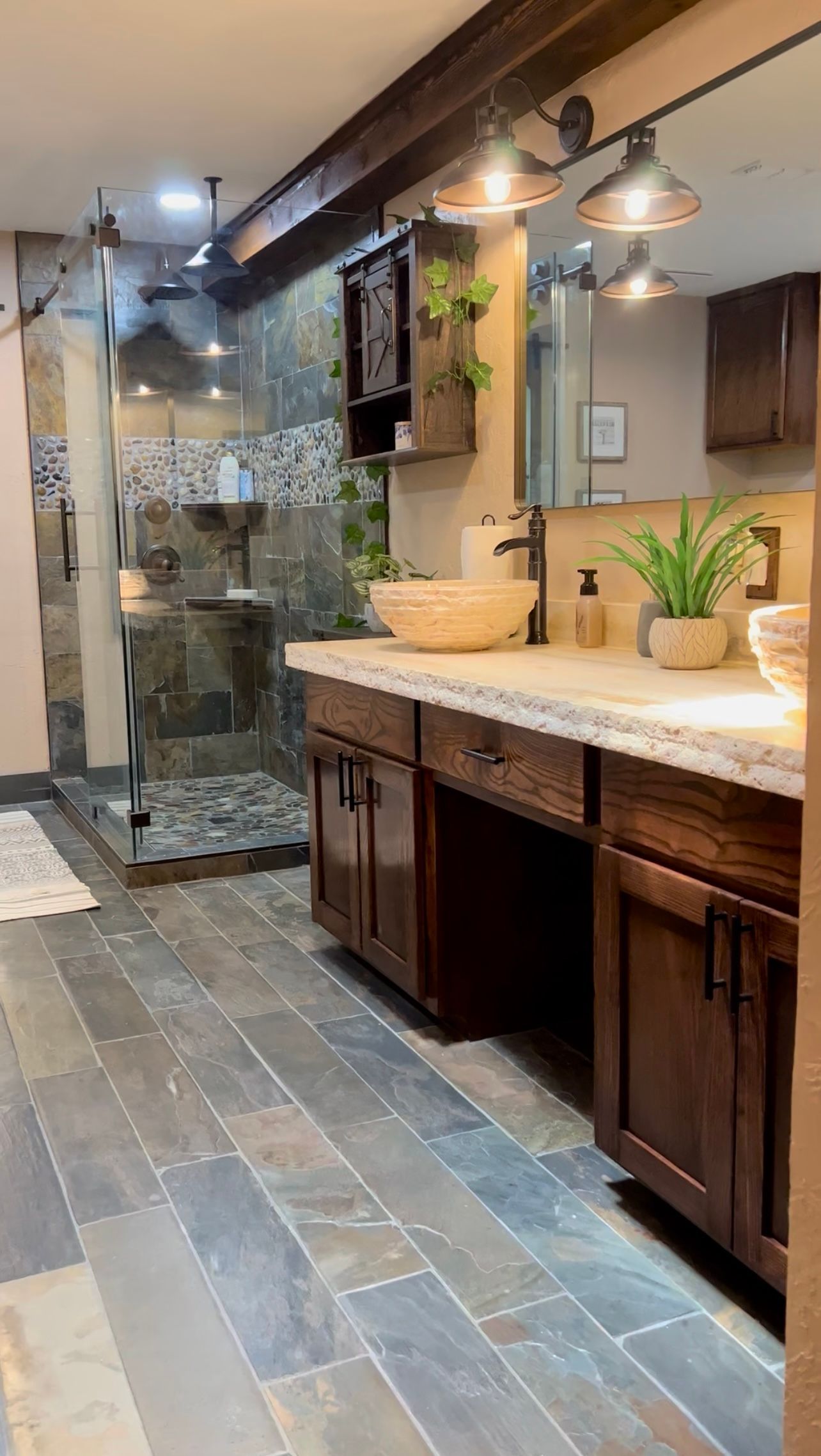 Rustic bathroom with dark wood cabinets, slate tile, glass shower, and stone walls.