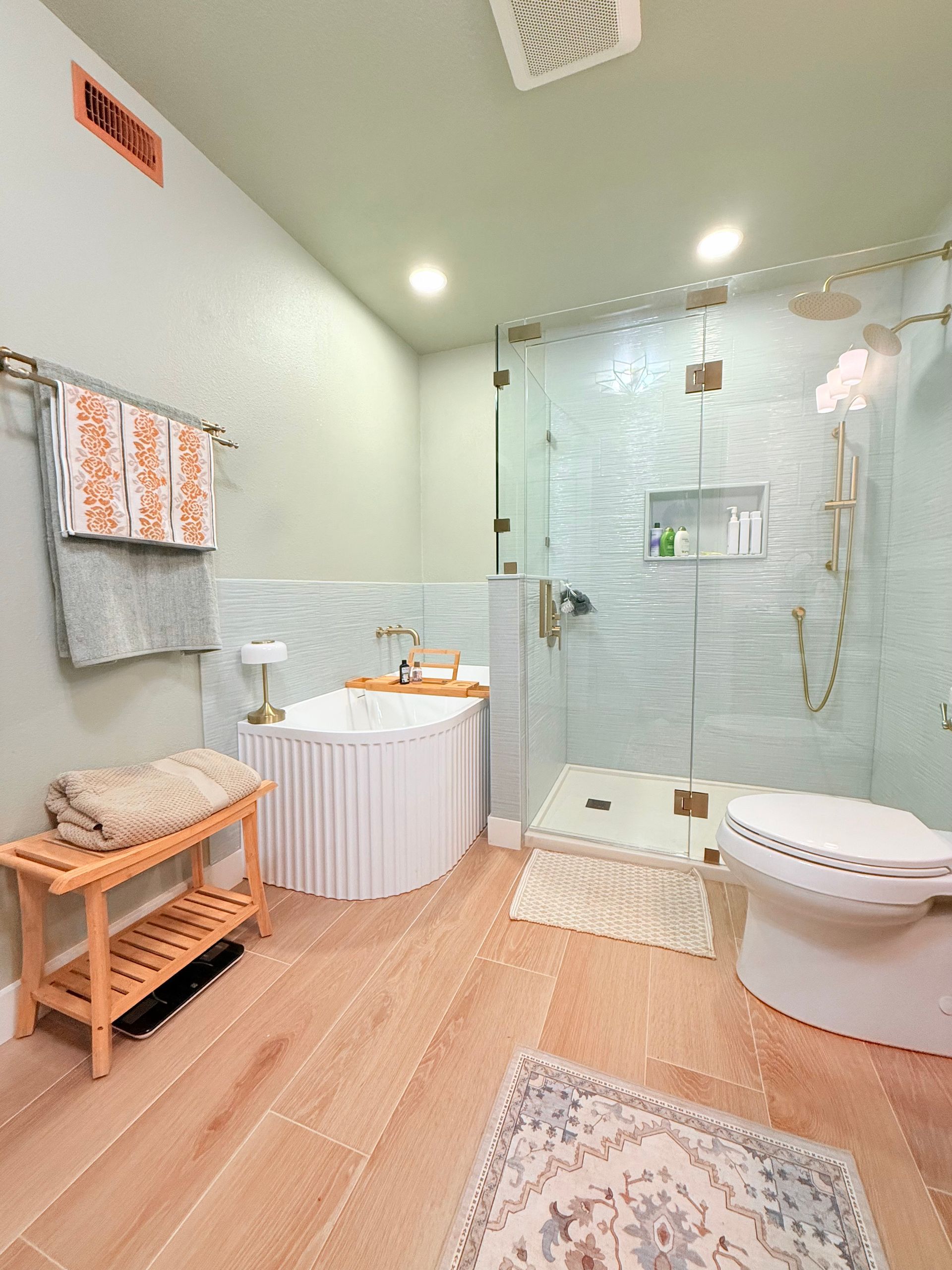Bright bathroom with a glass shower, soaking tub, wooden tile floor, and a toilet.