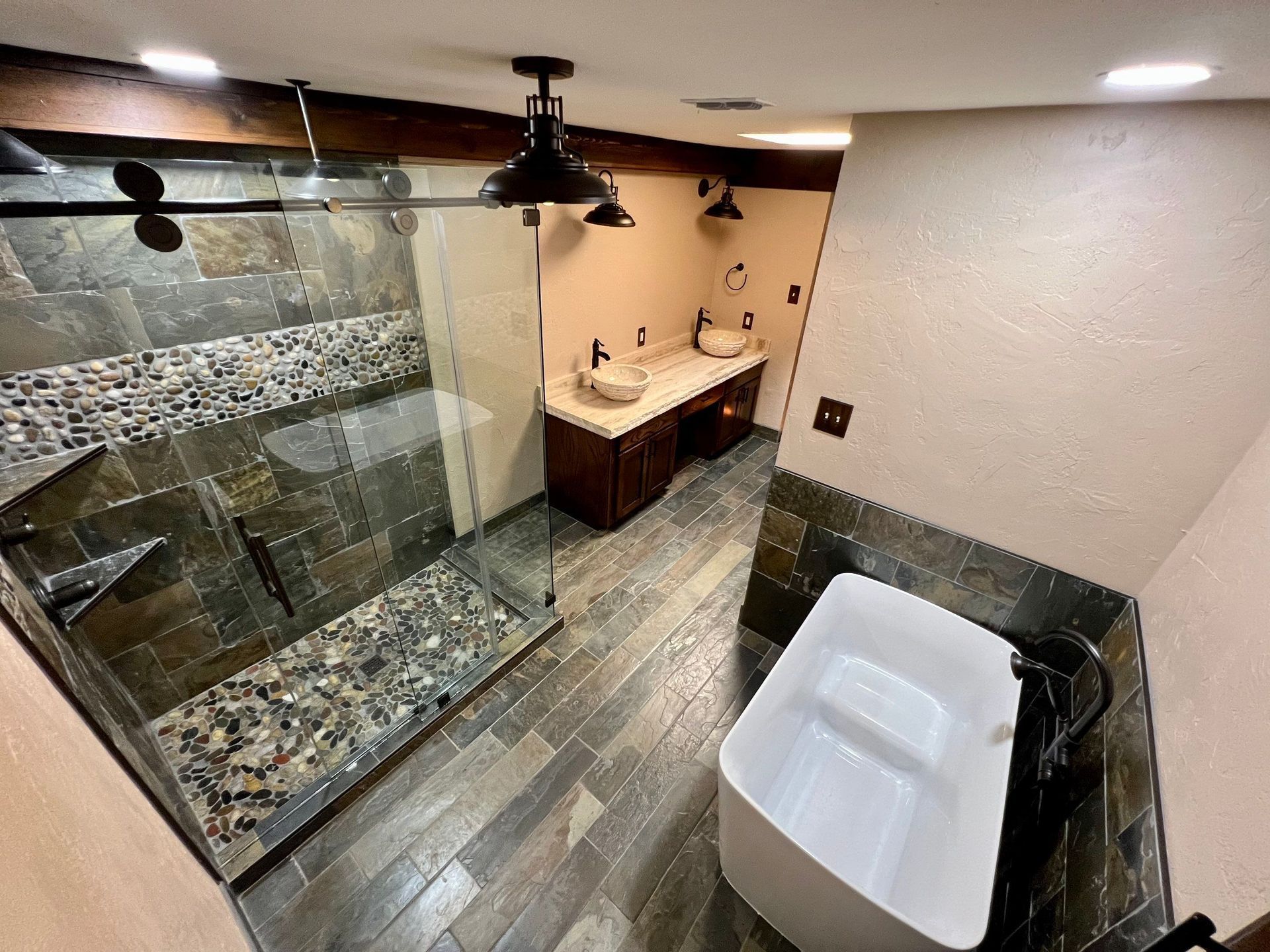 Bathroom with a tiled shower, freestanding tub, and double vanity. Dark wood elements and black fixtures.