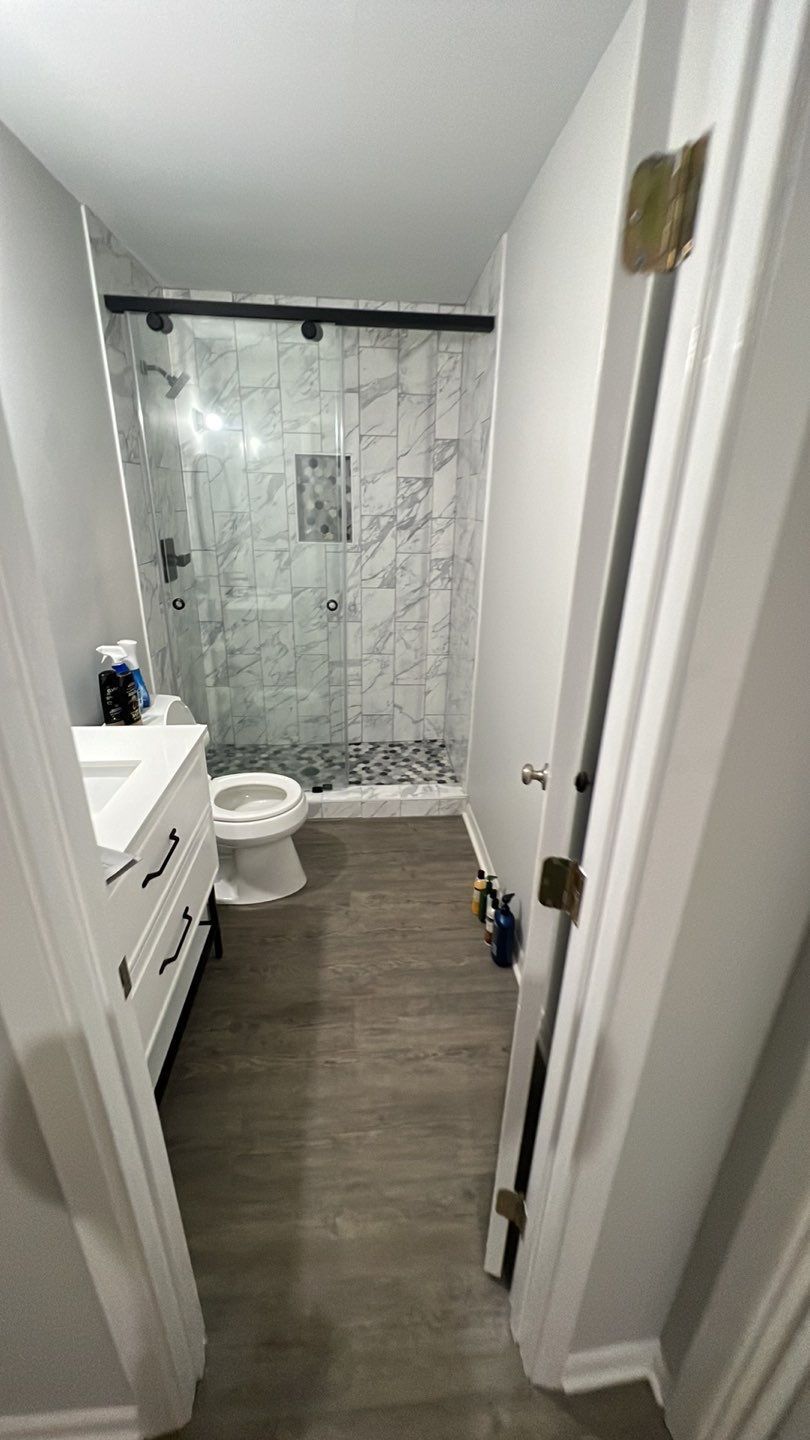 Bathroom with white vanity, toilet, glass shower, black fixtures, and gray flooring.