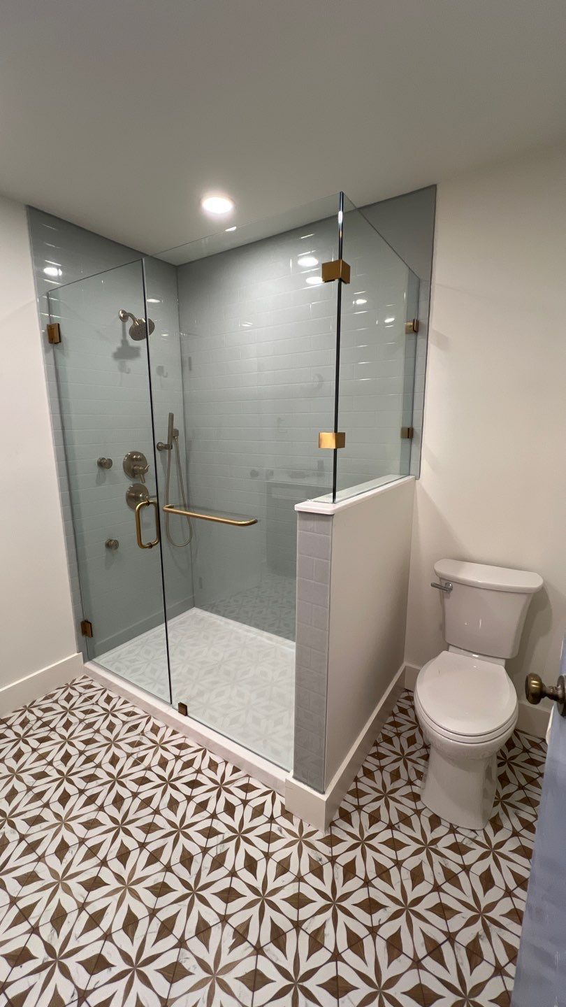 Bathroom with patterned floor, glass shower, gray tiled wall, and white toilet.