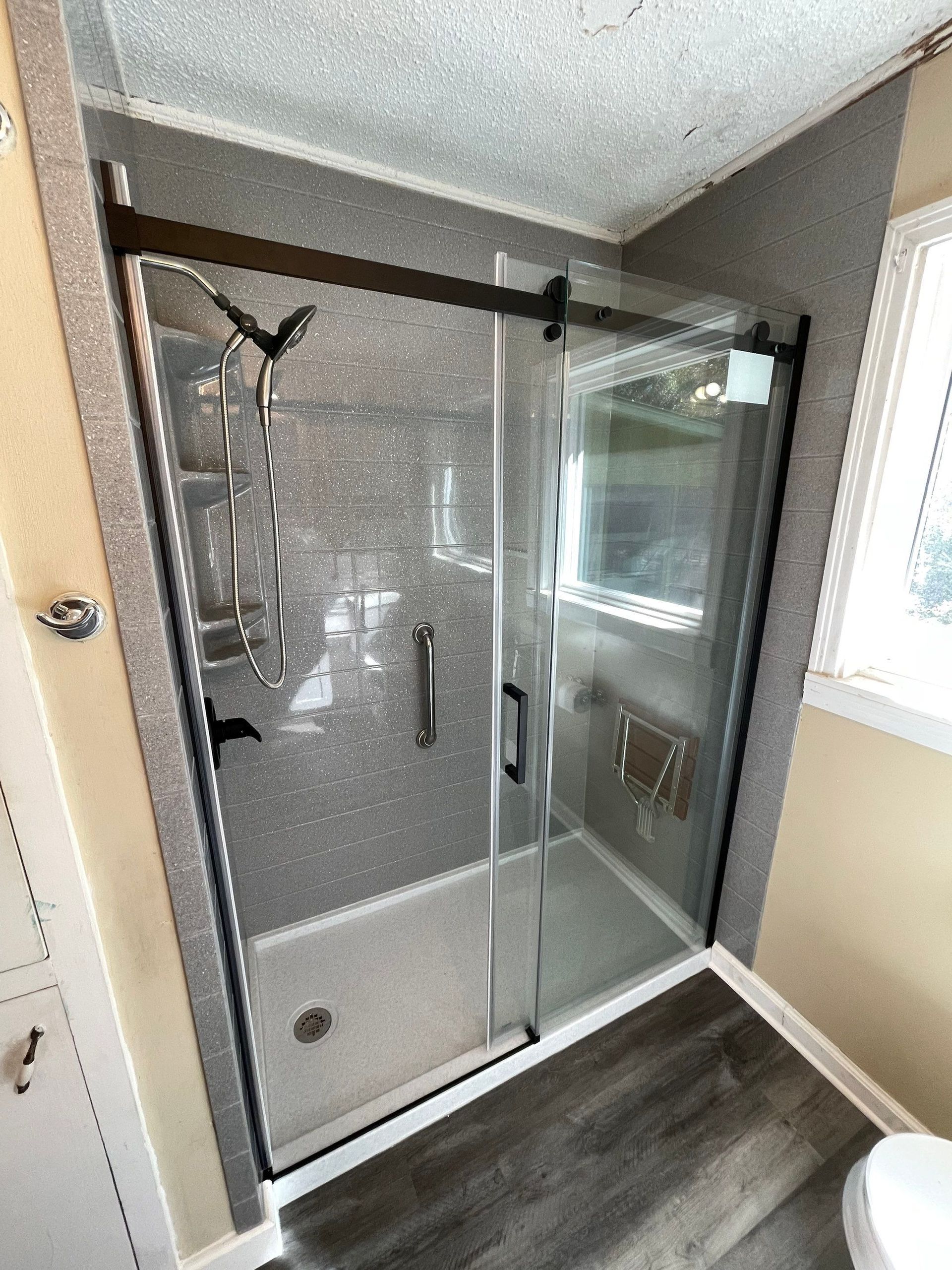 Modern shower with sliding glass door, black hardware, and gray tiled walls.