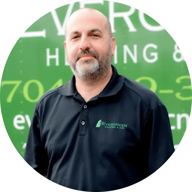 A person with a beard wearing a black polo shirt, standing in front of a green vehicle with company branding.