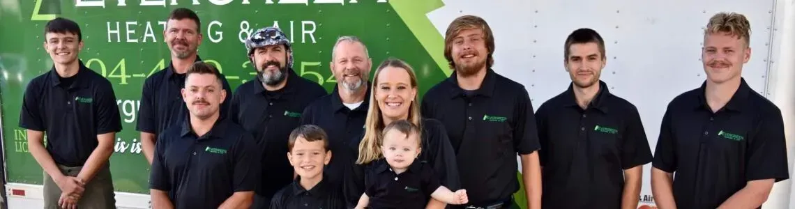 A group of employees in black polo shirts posing in front of an Evergreen Heating & Air branded truck.