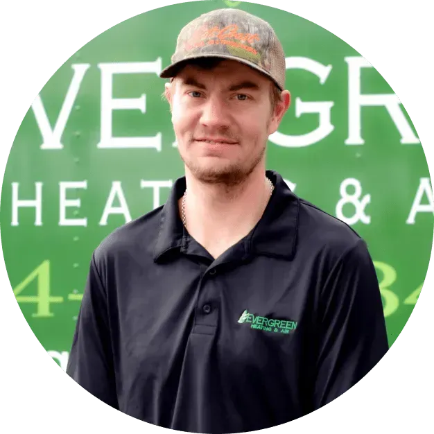 A person in a black polo shirt and camo hat posing in front of a green Evergreen Heating & Air vehicle.