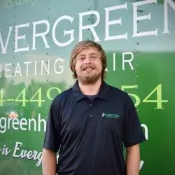 A person stands smiling in a dark polo shirt in front of a green Evergreen Heating & Air company vehicle.