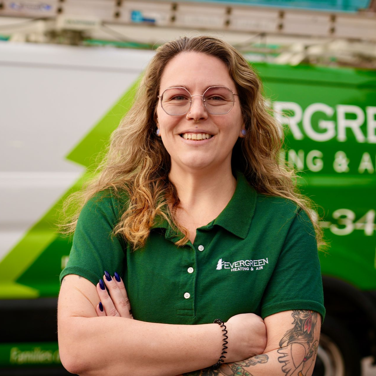 Smiling person in green polo standing before an Evergreen Heating & Air service van