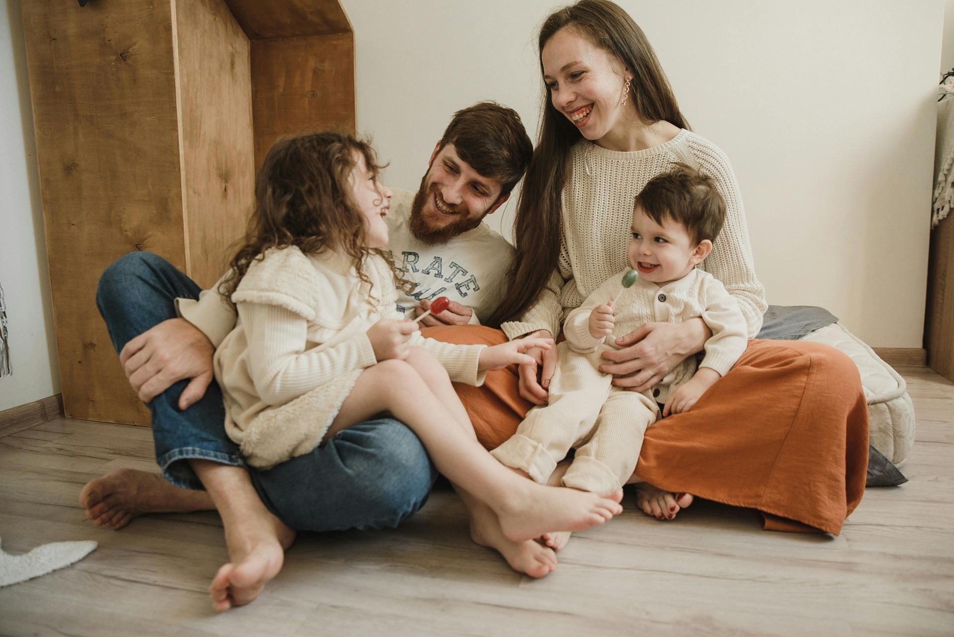 A family sitting on the floor indoors, laughing and interacting with two young children.