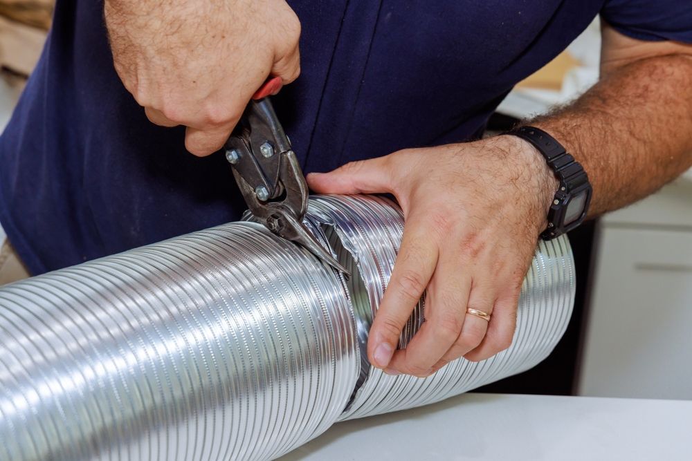 Hands using snips to cut through a metal dryer vent duct.