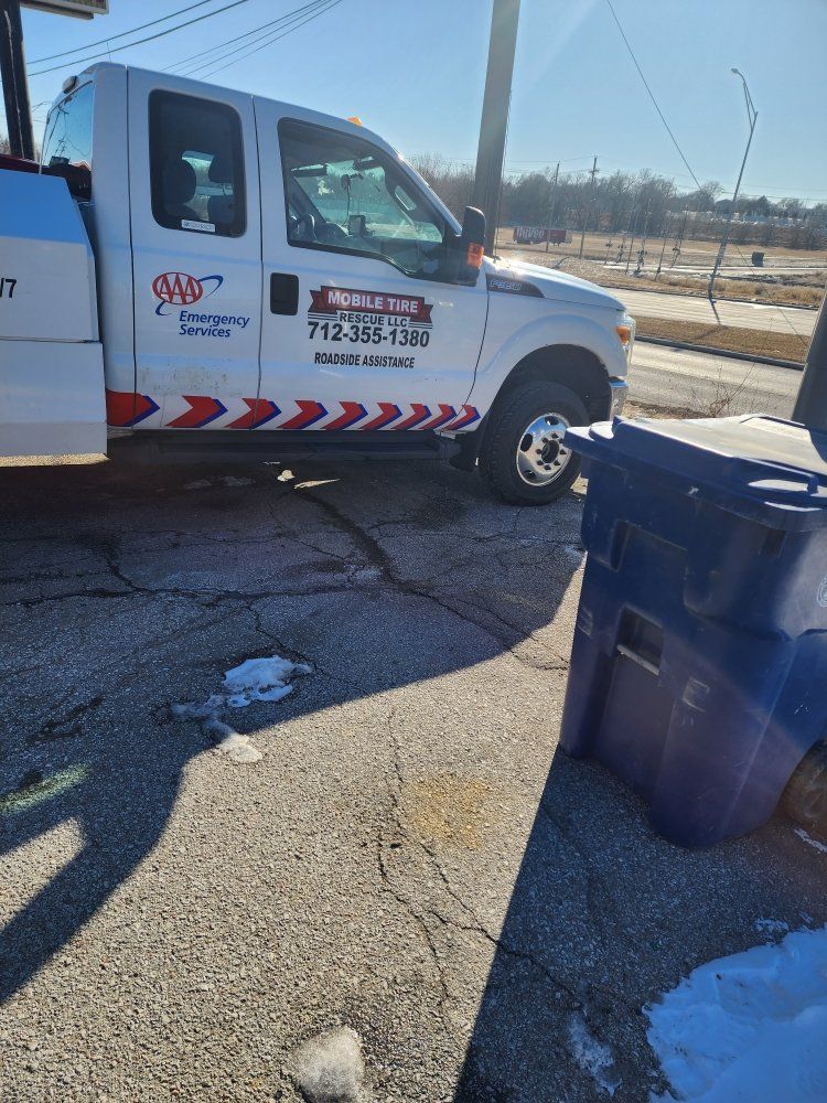 Tow truck parked on cracked pavement, sunny day. Truck has red and white logo with phone number.