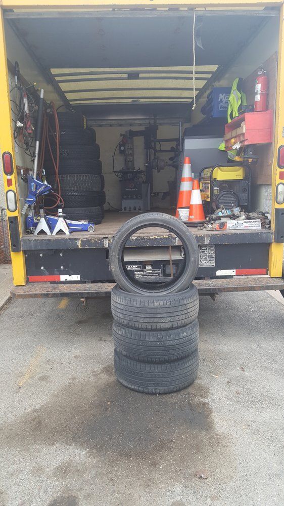 A tire service truck with a stack of tires in front. The truck is open, revealing tools and equipment inside.