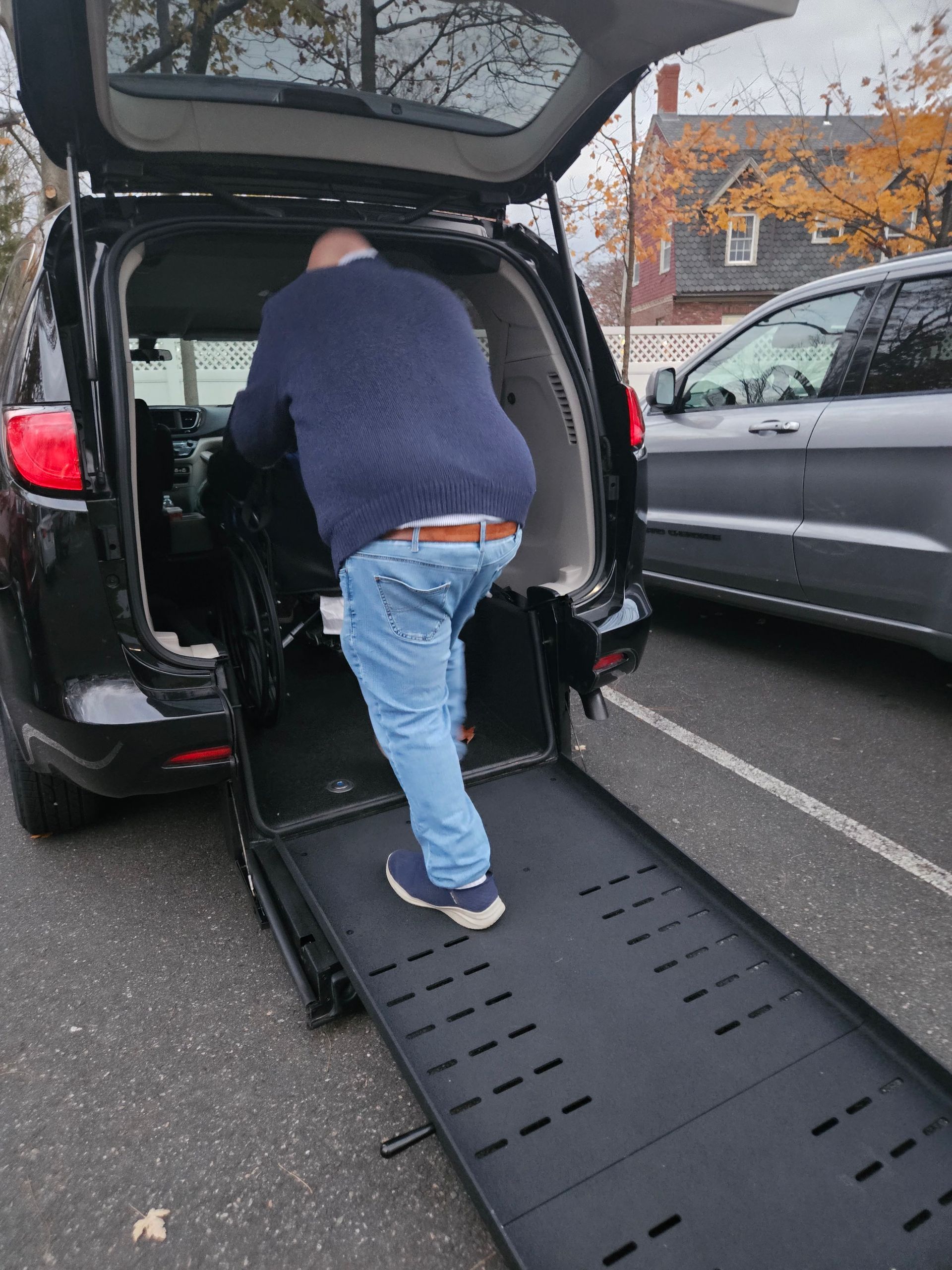 Person loading a black wheelchair-accessible van using a rear ramp on a wet street