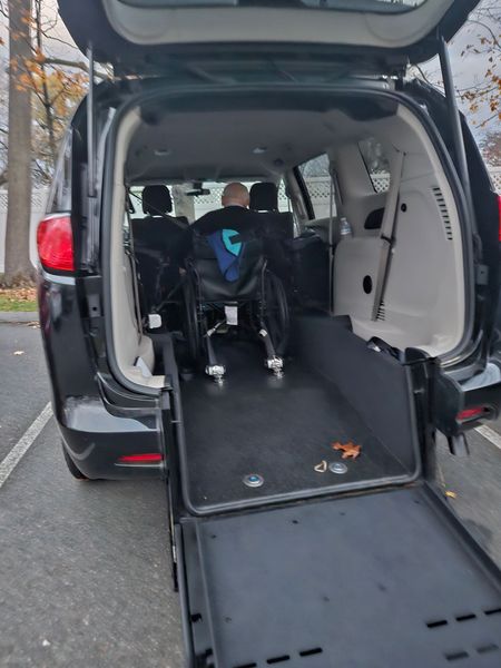 Open minivan with rear ramp deployed for wheelchair access, wheelchair inside cargo area.