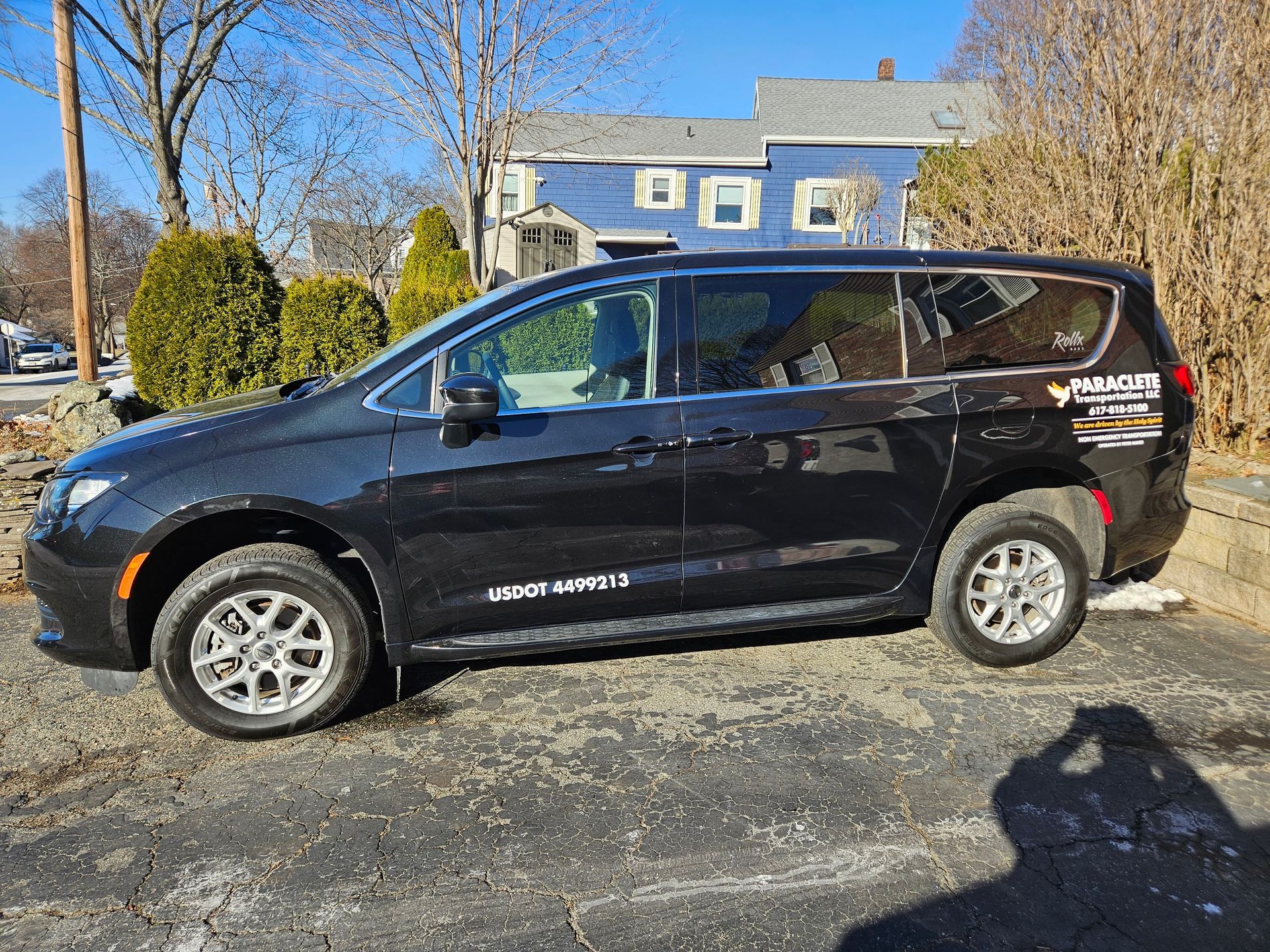 Black SUV parked on a driveway in front of a blue house on a sunny day