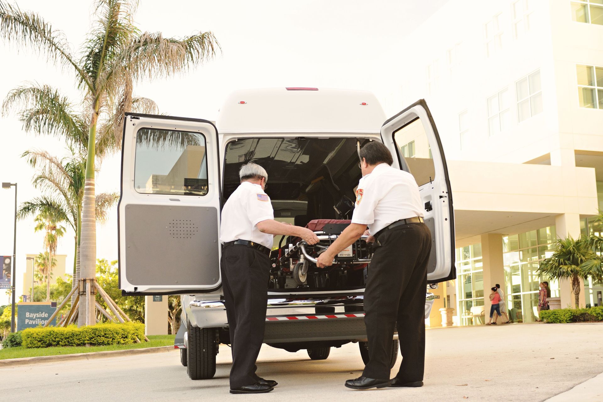 Two workers loading equipment into the back of a white van outside a building