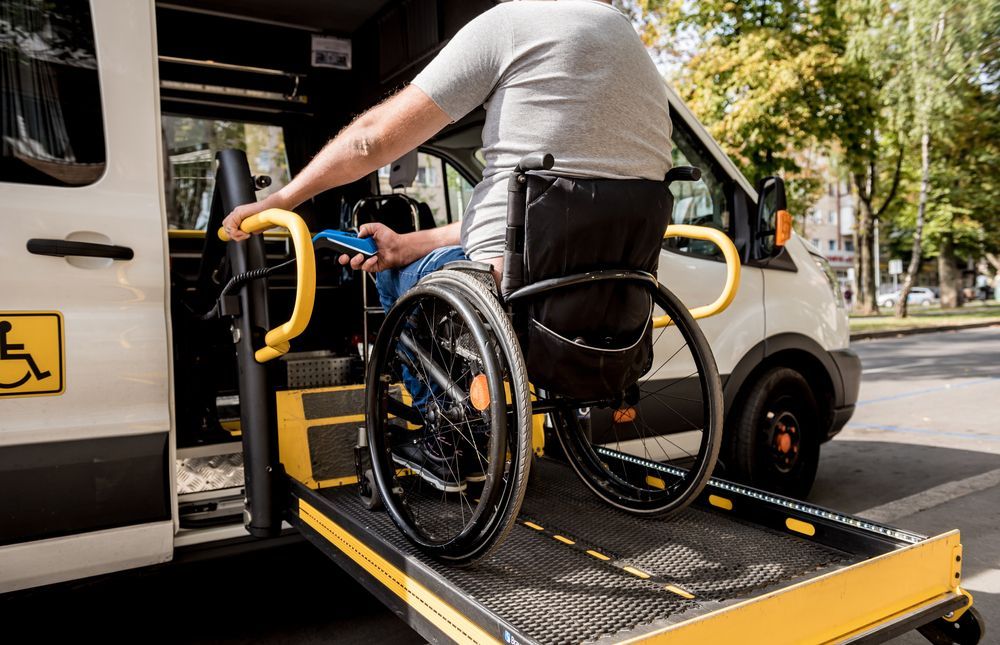 Wheelchair user boarding a van via a yellow wheelchair lift on a city street