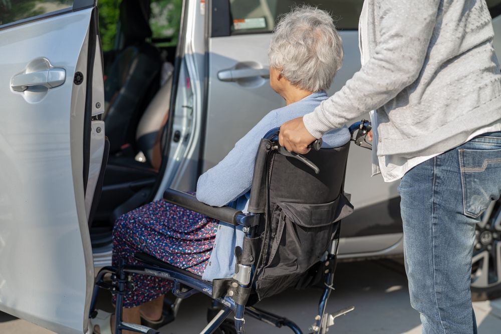 Person helping an older adult with a walker into a silver car