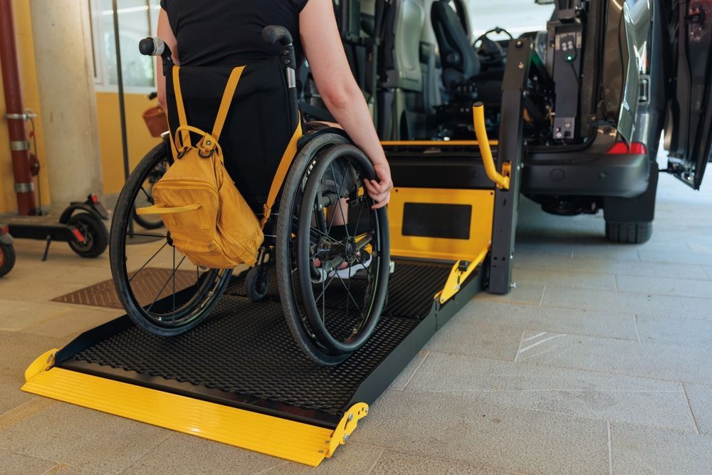 Person in a wheelchair on a yellow vehicle ramp inside a garage, with a car in the background