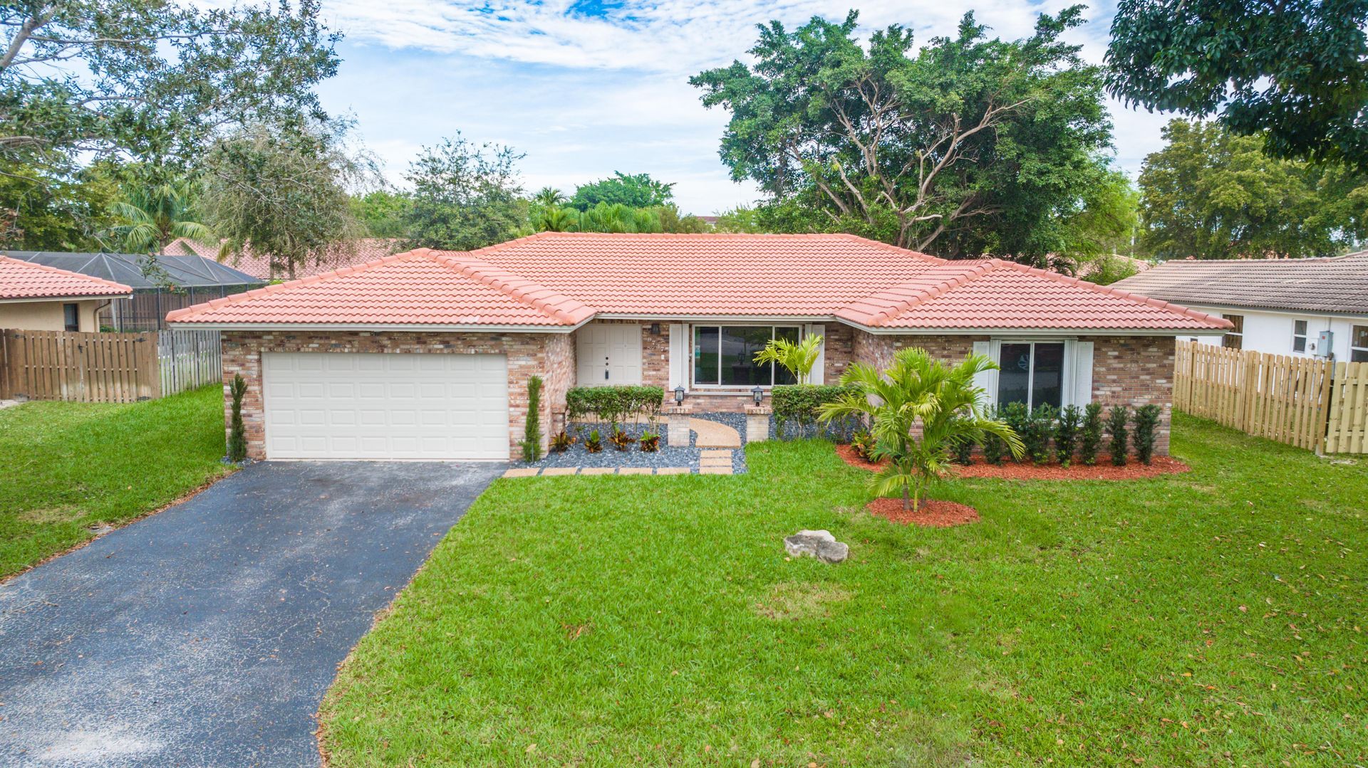 Single-story house with red tile roof, white garage, and green lawn in a suburban neighborhood