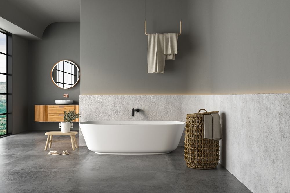 Minimalist modern bathroom with freestanding tub, gray walls, round mirror, and woven laundry basket