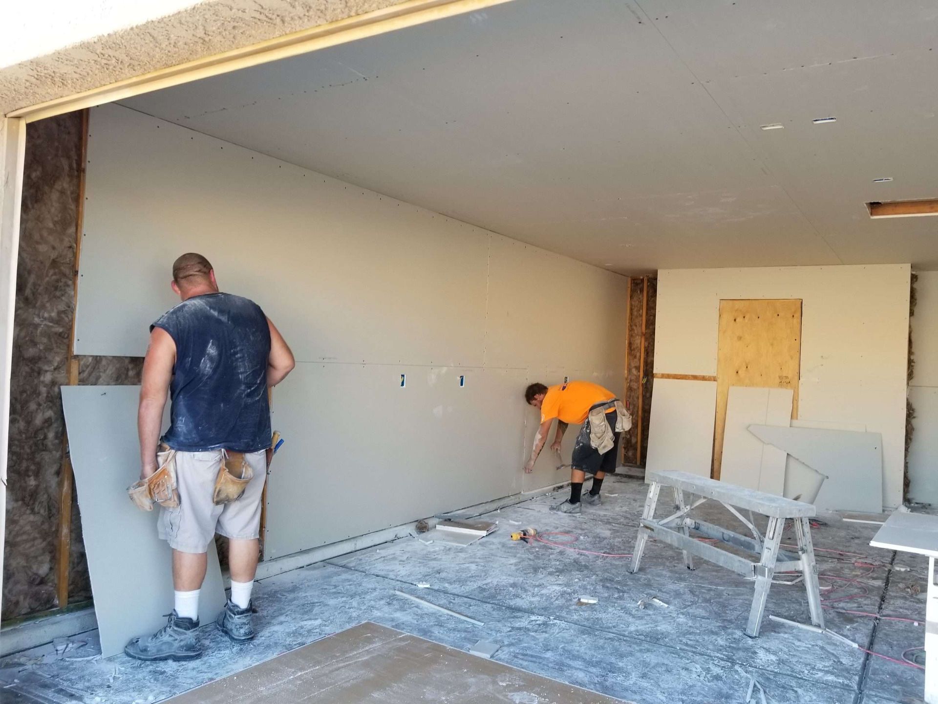 Two workers painting a room during renovation, with ladders, tools, and drywall patches visible.