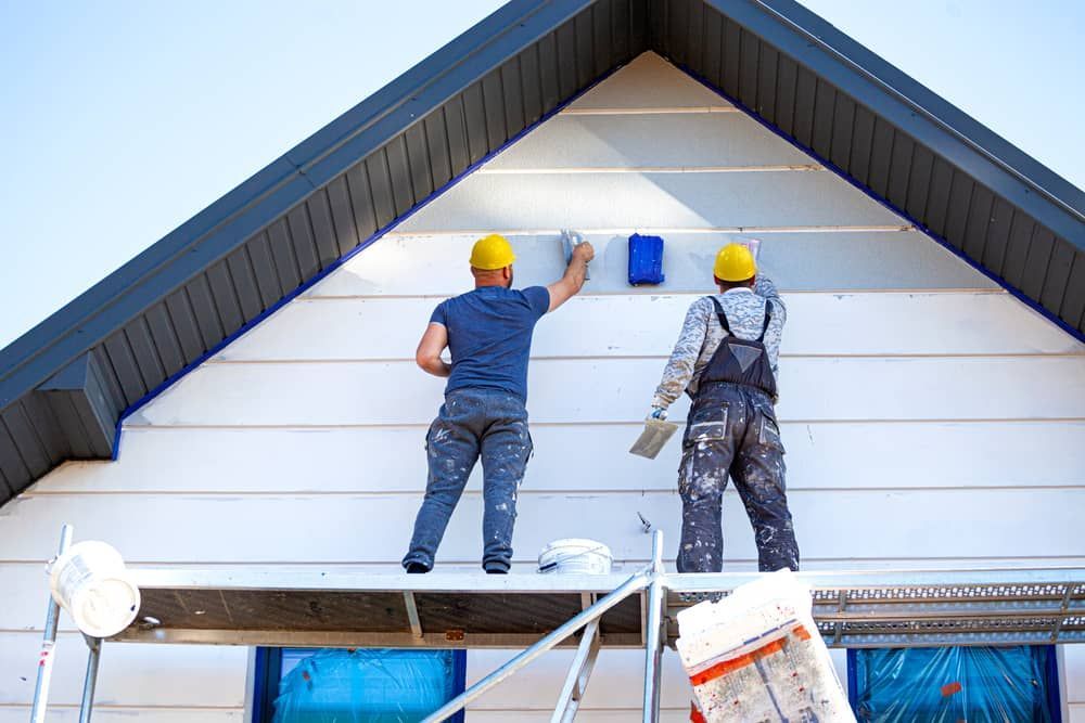 Two workers painting the exterior siding of a house beneath a dark roofline