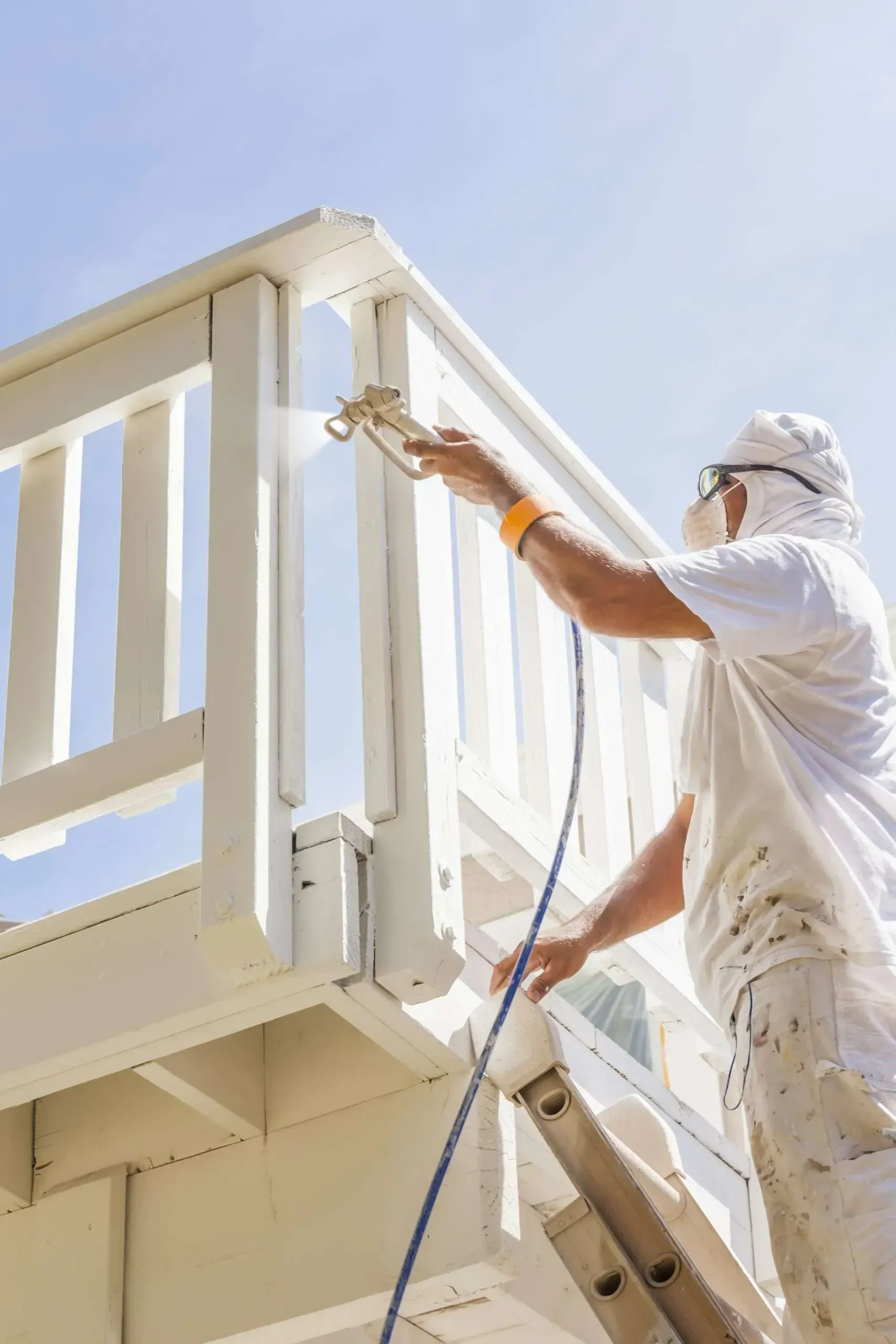 Painter on ladder painting a white balcony railing against a blue sky