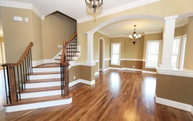 Spacious beige living room with hardwood floors, staircase, arched entryway, and white trim columns