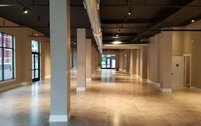 Empty modern office space with large windows, beige floors, and exposed ceiling ducts