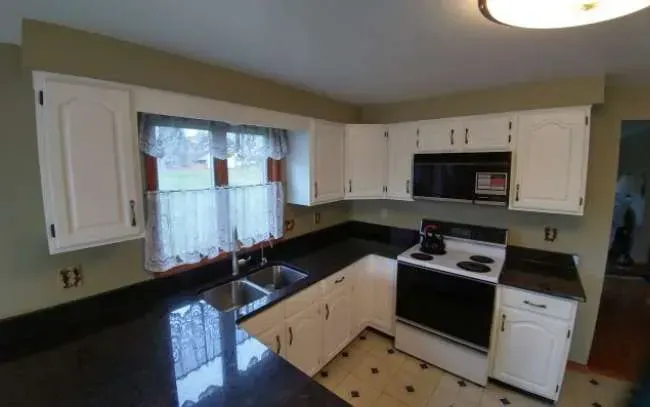 Bright kitchen with white cabinets, black countertops, tiled backsplash, window, and white stove and dishwasher.