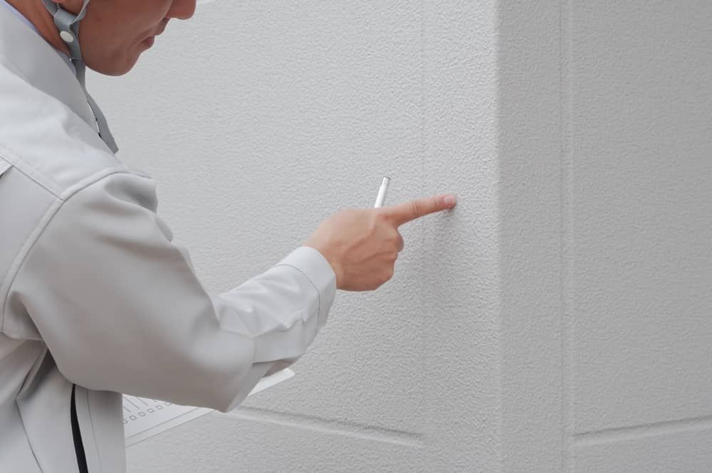 Person in a white shirt pointing at a textured white wall seam