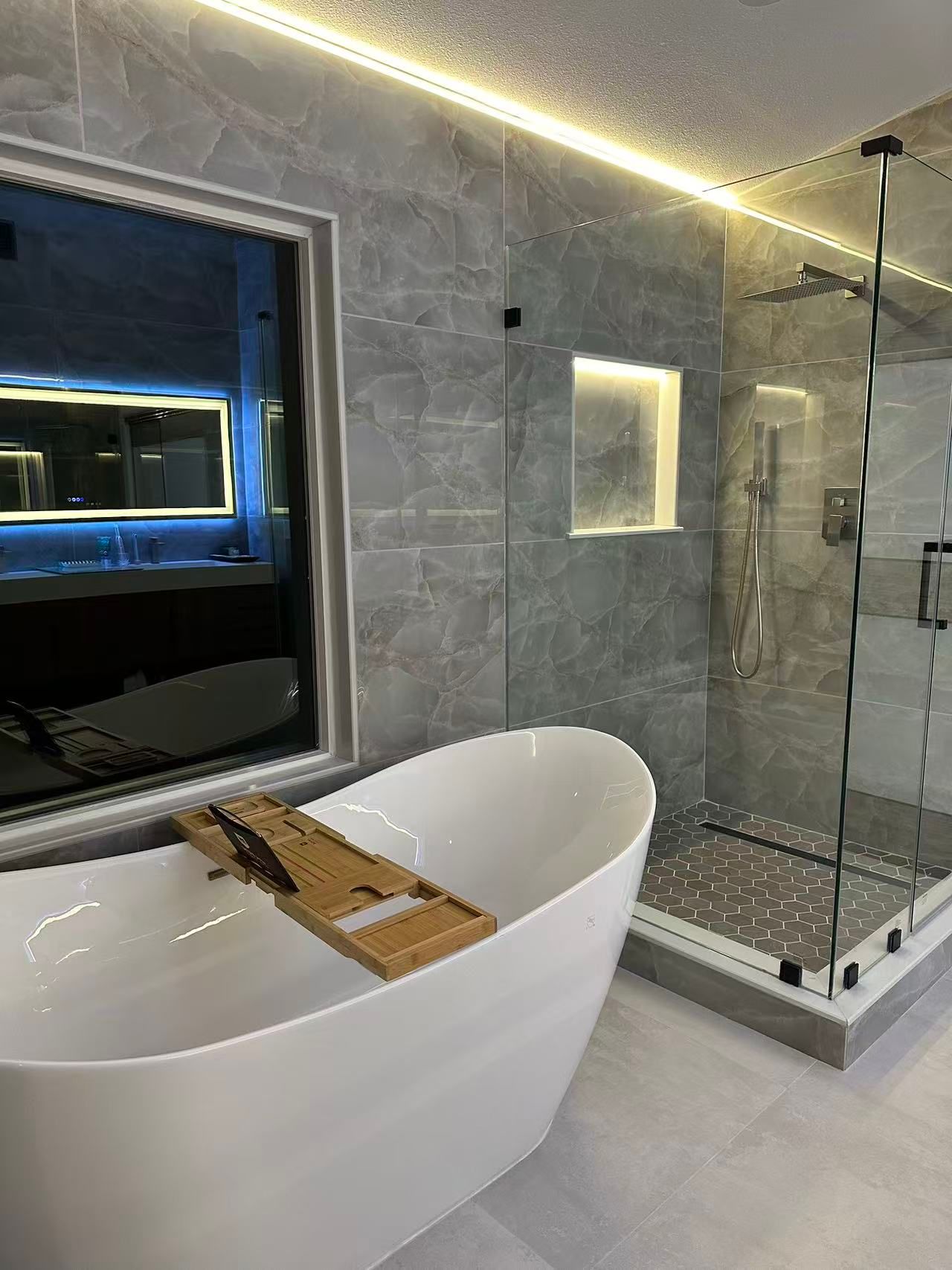 Modern bathroom with a white tub, shower, gray tile walls, and a window.