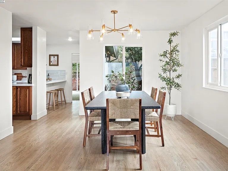 Dining room with a table, chairs, and a hanging light fixture. The room has light wood floors and white walls.