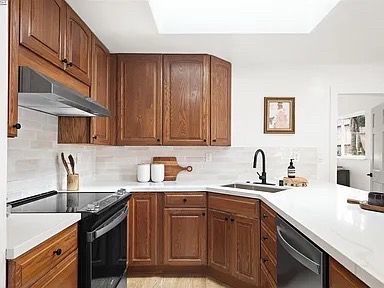 Kitchen with wood cabinets, white countertops, black appliances, and a black faucet.