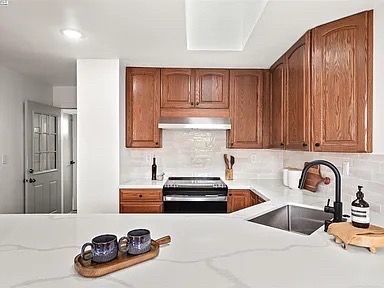 Kitchen with wood cabinets, white countertops, and a black stove. Cups on a tray in the foreground.